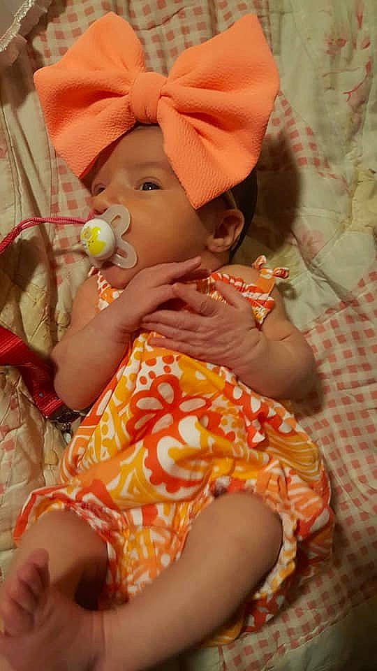 Alaska is registered to the contest to win money with this photo: arm, baby, baby_toddler_clothing, cheek, child, comfort, eye, hand, happy, human_body, lap, lip, mouth, nose, orange, pattern, person, pink, skin, textile