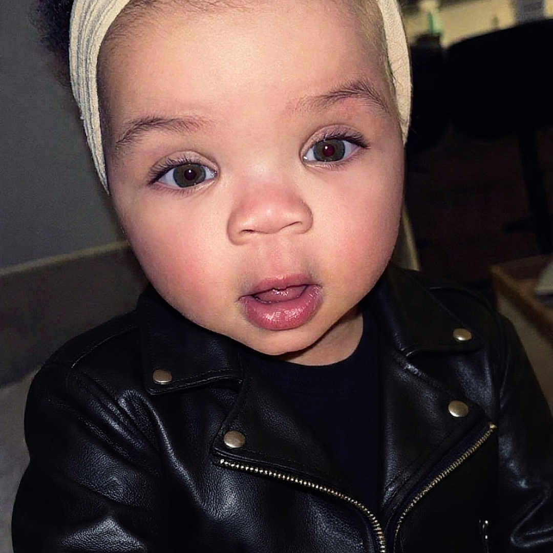 Kézia a rejoint le concours — aidez-le/la à gagner de superbes lots ! toddler, child, headband, bow, leather_jacket, toy, indoor, portrait, cute, expression, face, person, clothing, young_child, curly_hair, jacket, playing, baby, hand, closeup