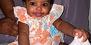 Rose-Shaina joined the competition — help win amazing prizes! baby, child, smiling, reaching, sock, floral_dress, bed, hand, adult, patterned_bedspread, cute, indoors, person, face, happy, infant, curly_hair, skin, sitting, support