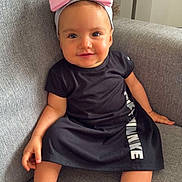 Aya a rejoint le concours — aidez-le/la à gagner de superbes lots ! baby, child, girl, smile, headband, pink_bow, black_dress, sitting, couch, grey_couch, barefoot, indoors, cute, portrait, happy, infant, young_child, comfortable, casual_clothing, home