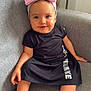 baby, child, girl, smile, headband, pink_bow, black_dress, sitting, couch, grey_couch, barefoot, indoors, cute, portrait, happy, infant, young_child, comfortable, casual_clothing, home