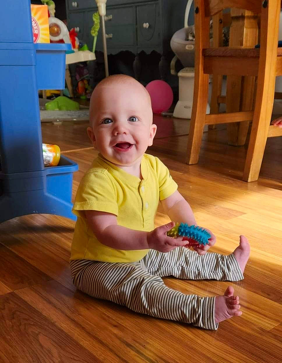 Ely is registered to the contest to win money with this photo: baby, baby_toddler_clothing, chair, child, floor, flooring, happy, hardwood, laminate_flooring, person, plank, room, sleeve, smile, standing, t_shirt, toddler, varnish, wood, wood_flooring