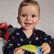 Anthony a rejoint le concours — aidez-le/la à gagner de superbes lots ! baby, child, clothing, couch, eyes, face, hand, happy, holding, indoor, onesie, packet, person, pillow, portrait, smiling, snack, star_pattern, toddler, young_child