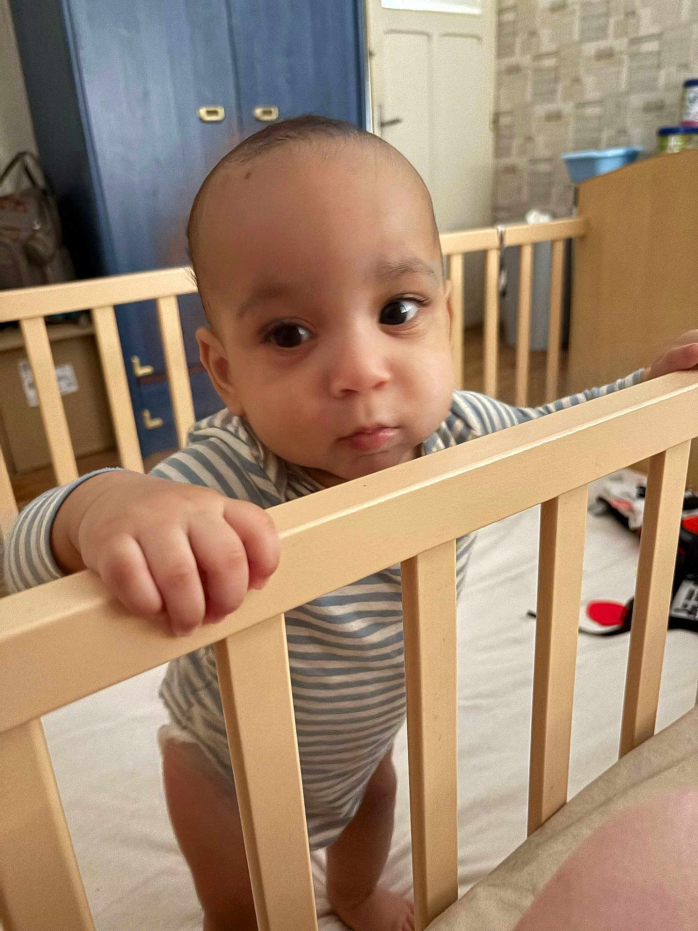 Léo a rejoint le concours — aidez-le/la à gagner de superbes lots ! baby, crib, hand, furniture, room, indoor, child, person, curious, standing, striped_clothing, wood, floor, door, cabinet, toy, home, expression, face, young