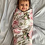 baby, smiling, floral_blanket, wrapped, bed, soft, hair, cute, child, lying_down, happy, portrait, indoors, infant, person, face, skin, hand, comfort, cozy