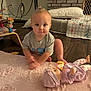 toddler, child, toy, doll, pink_rug, wooden_floor, quilt, pillow, gray_shirt, indoor, playtime, baby, floor, head, face, person, crawling, home, furniture, curious