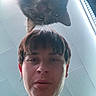 Wednesday is registered to the contest to win money with this photo: person, cat, selfie, indoor, ceiling, lighting, black_cat, young_man, portrait, looking_down, curious, casual, short_hair, neutral_expression, chain_necklace, tiled_ceiling, fluorescent_lighting, animal, pet, companion