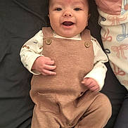 Elliot is registered to the contest to win money with this photo: baby, bed, blanket, casual, child, clothing, cozy, cute, fabric, face, hand, happy, infant, lying_down, overalls, person, portrait, smiling, soft, warm_colors