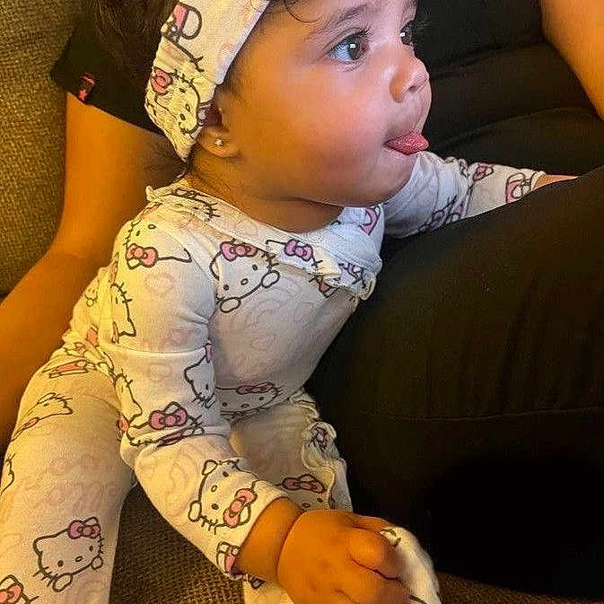 Sophia joined the competition — help win amazing prizes! toddler, child, pajamas, hello_kitty, headband, tongue_out, couch, sitting, person, childrens_clothing, cute, playful, indoor, fabric, texture, pink, white, pattern, face, hair