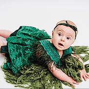 Kyndal joined the competition — help win amazing prizes! baby, infant, green_dress, headband, blanket, curious, wide_eyes, lying_down, white_background, portrait, child, cute, fuzzy, fabric, hands, feet, skin, expression, studio, photography