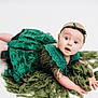baby, infant, green_dress, headband, blanket, curious, wide_eyes, lying_down, white_background, portrait, child, cute, fuzzy, fabric, hands, feet, skin, expression, studio, photography