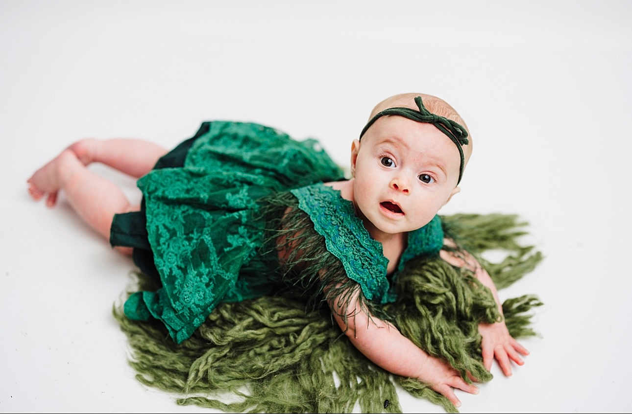 Kyndal joined the competition — help win amazing prizes! baby, infant, green_dress, headband, blanket, curious, wide_eyes, lying_down, white_background, portrait, child, cute, fuzzy, fabric, hands, feet, skin, expression, studio, photography