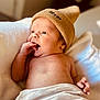 baby, newborn, hat, knit_hat, blanket, skin, infant, hand, face, portrait, lying_down, indoors, warm_light, cute, soft_texture, expression, child, person, cozy, relaxed