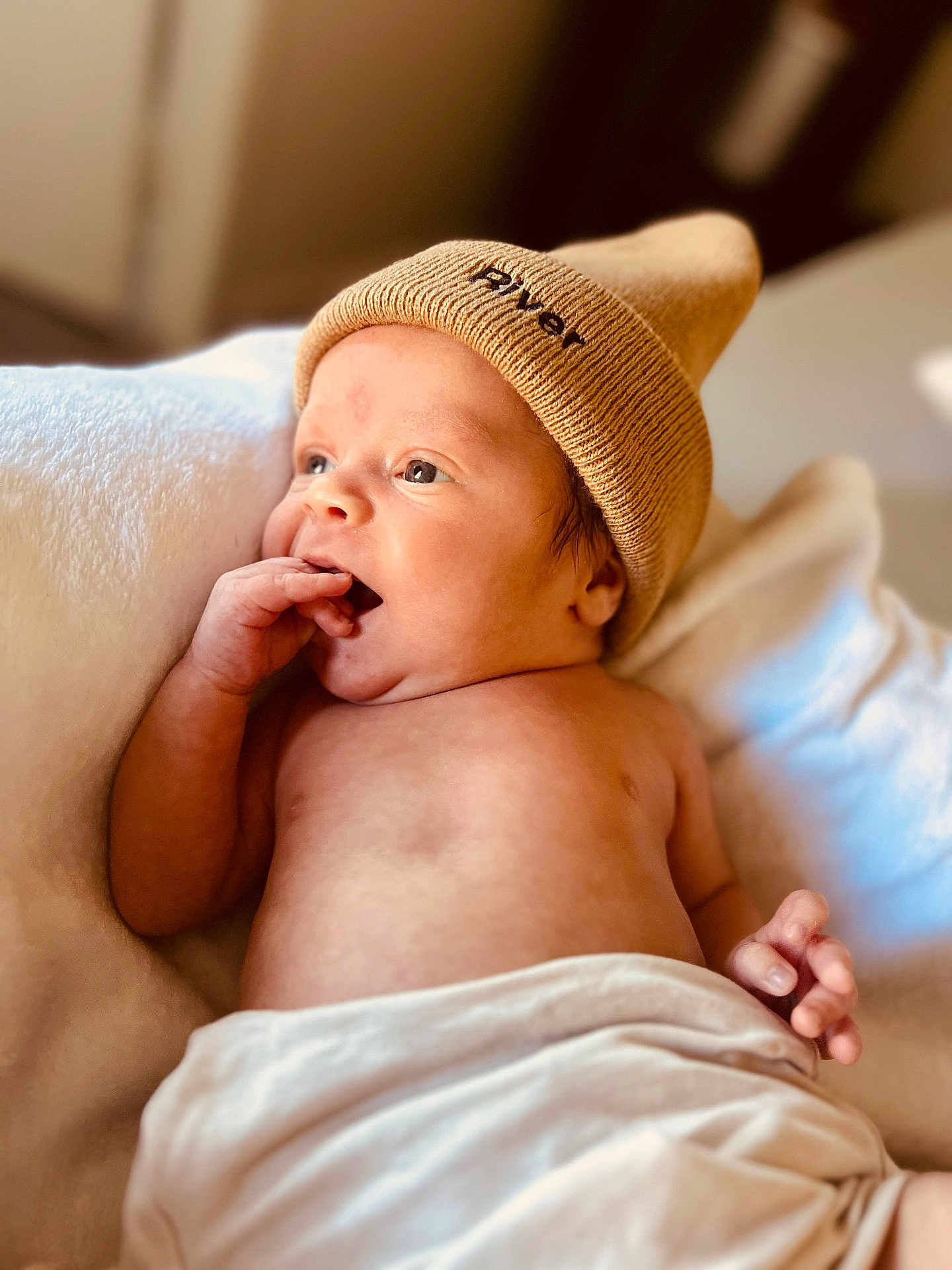 River is registered to the contest to win money with this photo: baby, newborn, hat, knit_hat, blanket, skin, infant, hand, face, portrait, lying_down, indoors, warm_light, cute, soft_texture, expression, child, person, cozy, relaxed