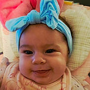 Skylar joined the competition — help win amazing prizes! baby, child, face, headband, bow, smiling, tongue, cute, infant, clothing, pattern, cushion, indoor, portrait, closeup, happy, young_child, headwear, soft_toys, cozy