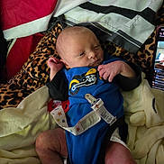 Colton is registered to the contest to win money with this photo: newborn, baby, infant, child, portrait, lying_down, blue_outfit, blanket, bedding, leopard_print, pacifier, pacifier_clip, hospital_bracelet, hands, feet, face, eyes_open, indoors, smartphone, cozy