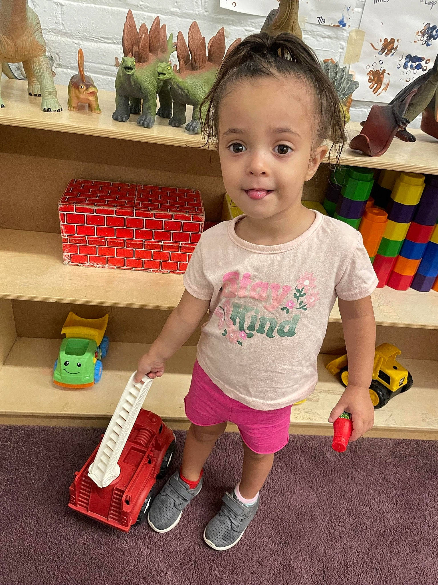 Myla is registered to the contest to win money with this photo: baby, baby_toddler_clothing, child, floor, flooring, fun, happy, human_leg, magenta, person, play, retail, shelf, shelving, shorts, sleeve, standing, t_shirt, toddler, vacation