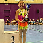 Mylana a rejoint le concours — aidez-le/la à gagner de superbes lots ! child, girl, gymnast, trophy, podium, gymnasium, competition, sport, medal, floor, group, audience, purple_wall, smile, dancewear, performance, team, event, young_athlete, indoor