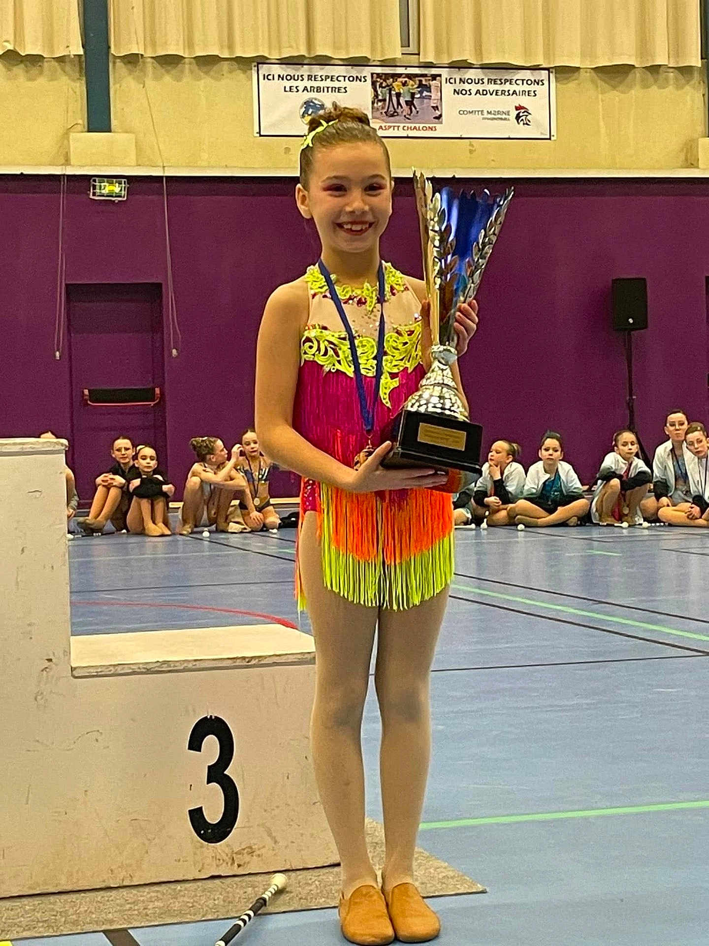 Mylana a rejoint le concours — aidez-le/la à gagner de superbes lots ! child, girl, gymnast, trophy, podium, gymnasium, competition, sport, medal, floor, group, audience, purple_wall, smile, dancewear, performance, team, event, young_athlete, indoor