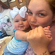 Oakleigh joined the competition — help win amazing prizes! baby, child, woman, tattoo, bow, smile, holding, hand, indoor, portrait, casual, clothing, table, background, person, cute, happy, face, blue_clothing, freckles