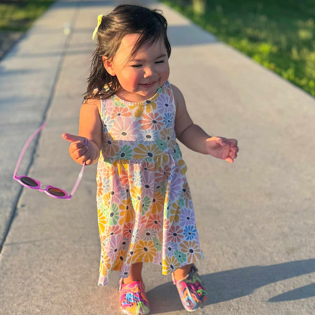 Milli is registered to the contest to win money with this photo: casual, child, colorful_dress, floral_pattern, girl, grass, happy, outdoor, person, playful, portrait, shoes, sidewalk, smiling, summer, sunglasses, sunlight, toddler, trees, walking