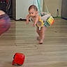 baby, child, indoor, wooden_floor, jumper, toy, red_toy, curious, playing, floor, child_safety, household, furniture, baby_clothes, childhood, exploration, suspended, toddler, flooring, home