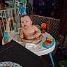 Adam is registered to the contest to win money with this photo: baby, activity_center, child, indoor, toy, plastic, face, furniture, play_area, gate, household_items, colorful, person, infant, seat, table, blur, curious, messy, room