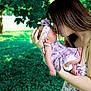 baby, woman, kiss, outdoor, nature, greenery, floral_dress, headband, affection, mother, child, love, portrait, holding, sunlight, grass, tree, tenderness, closeup, family