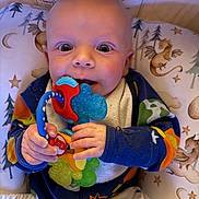 Jaxon joined the competition — help win amazing prizes! baby, infant, teething_toy, colorful, wide_eyes, cushion, dragon_pattern, onesie, hand, face, expression, indoor, cute, child, playful, soft_lighting, close_up, pale_skin, smiling, seated