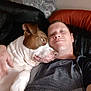 affection, animal, brown_and_white, casual, closeup, clothing, comfort, companion, couch, dog, earring, friendship, human, indoor, leisure, man, pet, portrait, relaxation, smile