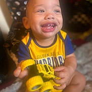 Royal is registered to the contest to win money with this photo: toddler, child, smiling, happy, toy, yellow_toy, truck, clothing, golden_state_warriors, shirt, face, hands, sitting, indoor, person, cute, baby, playing, expression, joy