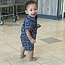toddler, child, barefoot, indoor, floor, shopping_cart, machine, tile_floor, blue_outfit, smiling, walking, curious, store, background, young_child, person, standing, happy, shorts, patterned_clothing