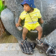 Malick participe au concours pour gagner de l'argent avec cette photo : bucket_hat, child, concrete, curious, daylight, expression, footwear, gorilla, hand, hat, outdoor, playful, sandals, sculpture, side_view, sitting, statue, toddler, urban, yellow_clothing