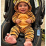 baby, child, car_seat, tiger_onesie, smiling, cute, infant, hooded_clothing, footwear_bare, indoor, happy, person, plush, cozy, seated, wood_floor, orange, black_stripes, adorable, small_feet
