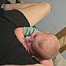 Skyler is registered to the contest to win money with this photo: baby, infant, pacifier, arm, skin, tattoo, shorts, indoor, wall, hole_in_wall, wood, blanket, person, resting, casual, clothing, head, face, child, comfort