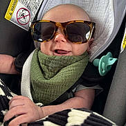 Nash joined the competition — help win amazing prizes! baby, sunglasses, car_seat, pacifier, green_bib, blanket, smile, infant, child, clothing, seatbelt, headwear, accessory, portrait, cute, indoor, face, hand, comfort, relaxing