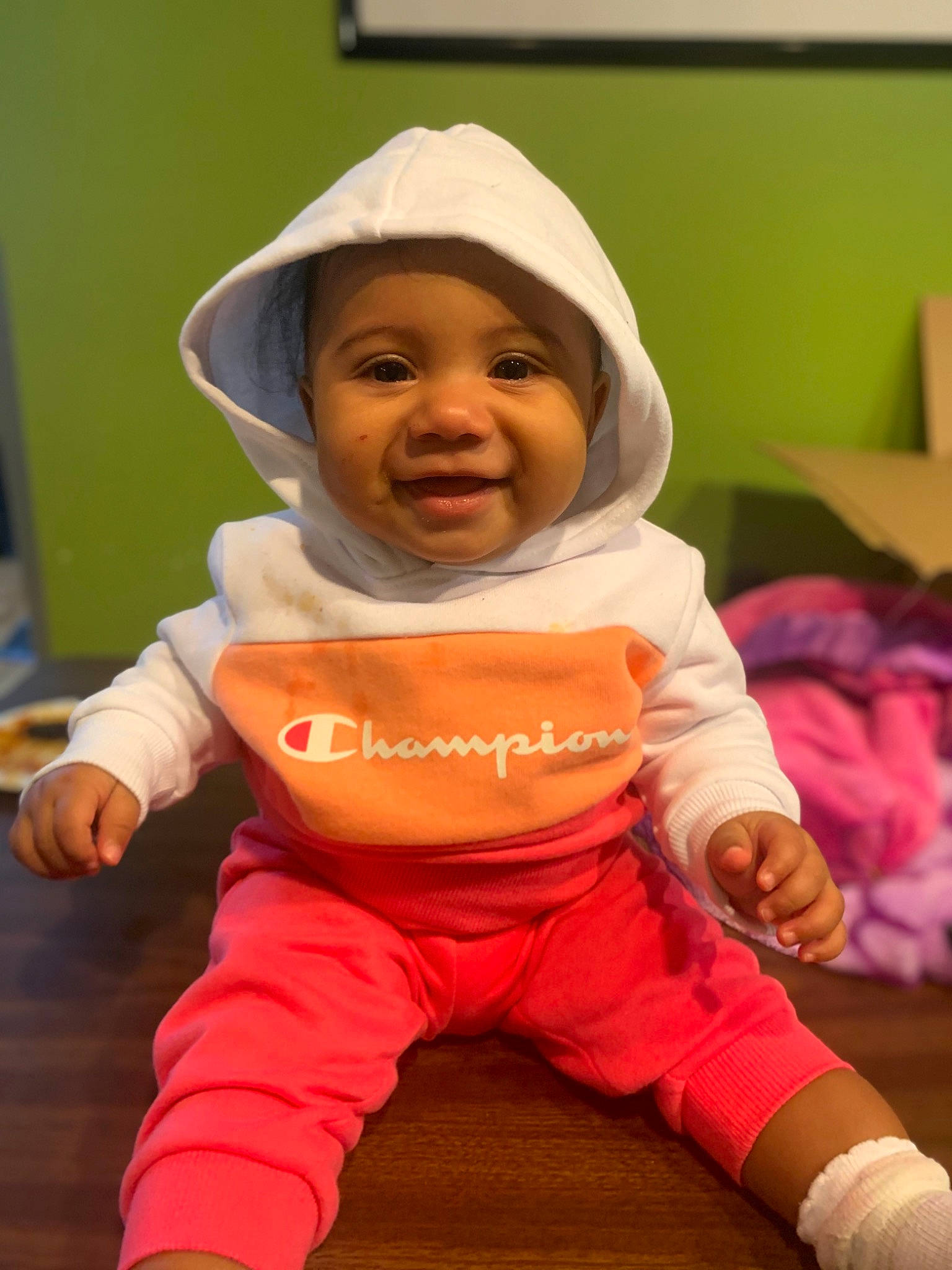 Venus is registered to the contest to win money with this photo: baby, baby_safety, baby_toddler_clothing, bib, cheek, comfort, finger, flooring, fun, happy, headwear, human_body, mouth, nose, person, pink, skin, sleeve, smile, t_shirt