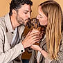 man, woman, puppy, dog, dachshund, pet, love, affection, holding, kissing, portrait, indoor, beige_background, casual_clothing, couple, cute, hands, long_hair, curly_hair, jeans