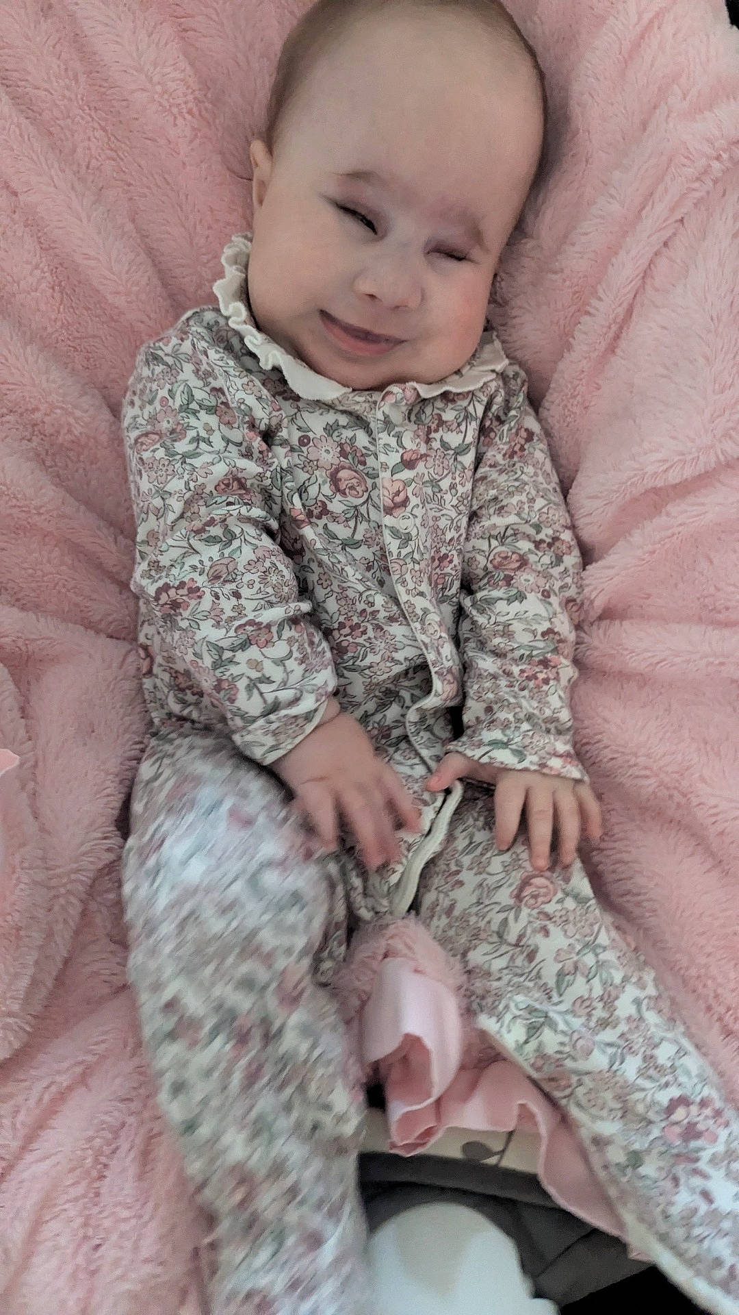 baby, baby_girl, child, comfort, cozy, cute, expression, fabric, face, floral_clothing, hand, indoor, infant, onesie, pink_blanket, portrait, sitting, smile, soft_texture, young_child