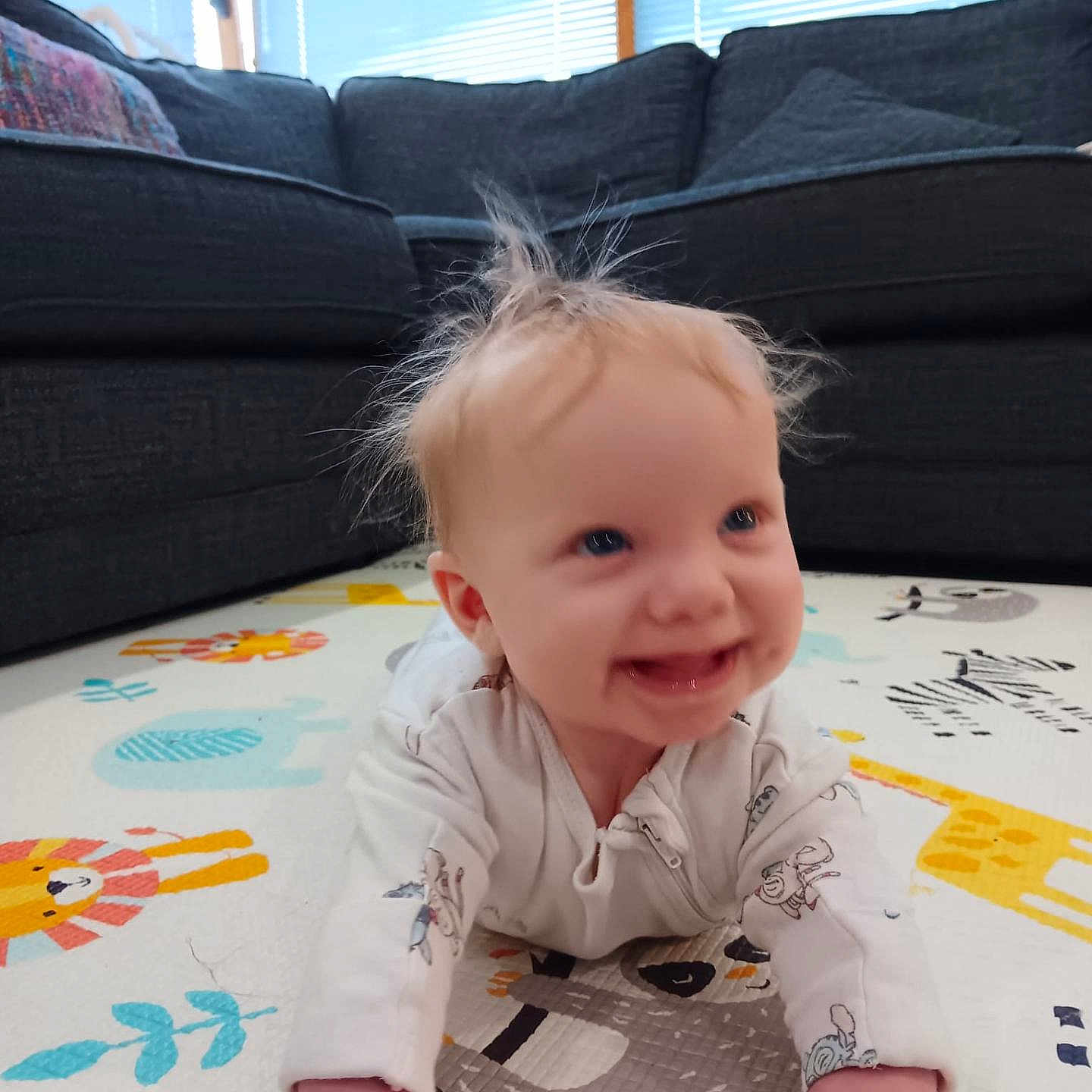 Ella Reilly is registered to the contest to win money with this photo: animal_print, baby, blonde_hair, child, clothing, couch, crawling, cute, floor, happy, home, indoor, infant, living_room, person, play_mat, portrait, smiling, soft_light, window_blinds