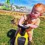 Henry joined the competition — help win amazing prizes! toddler, child, toy_car, yellow, grass, outdoor, sunny, red_hair, rosy_cheeks, playground, hay_bales, steering_wheel, shorts, shirt, shoes, summer, daytime, curious, playing, fun