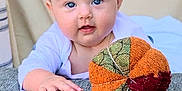 Nova is registered to the contest to win money with this photo: baby, infant, blue_eyes, plush_toy, orange, green, red, hand, crawling, texture, fabric, white_clothing, indoor, portrait, cute, child, soft_light, background, smiling, curious