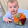 baby, infant, blue_eyes, plush_toy, orange, green, red, hand, crawling, texture, fabric, white_clothing, indoor, portrait, cute, child, soft_light, background, smiling, curious