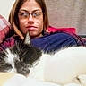 person, cat, glasses, sleeping, black_and_white_cat, blanket, couch, indoor, plaid, resting, cozy, relaxed, furniture, portrait, face, home, casual, comfort, animal, pet
