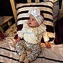 Naëlya a rejoint le concours — aidez-le/la à gagner de superbes lots ! baby, child, infant, headband, bow, clothing, floral_pattern, sitting, bed, pillow, striped, smile, cute, cozy, indoors, person, soft_lighting, fabric, socks, happy