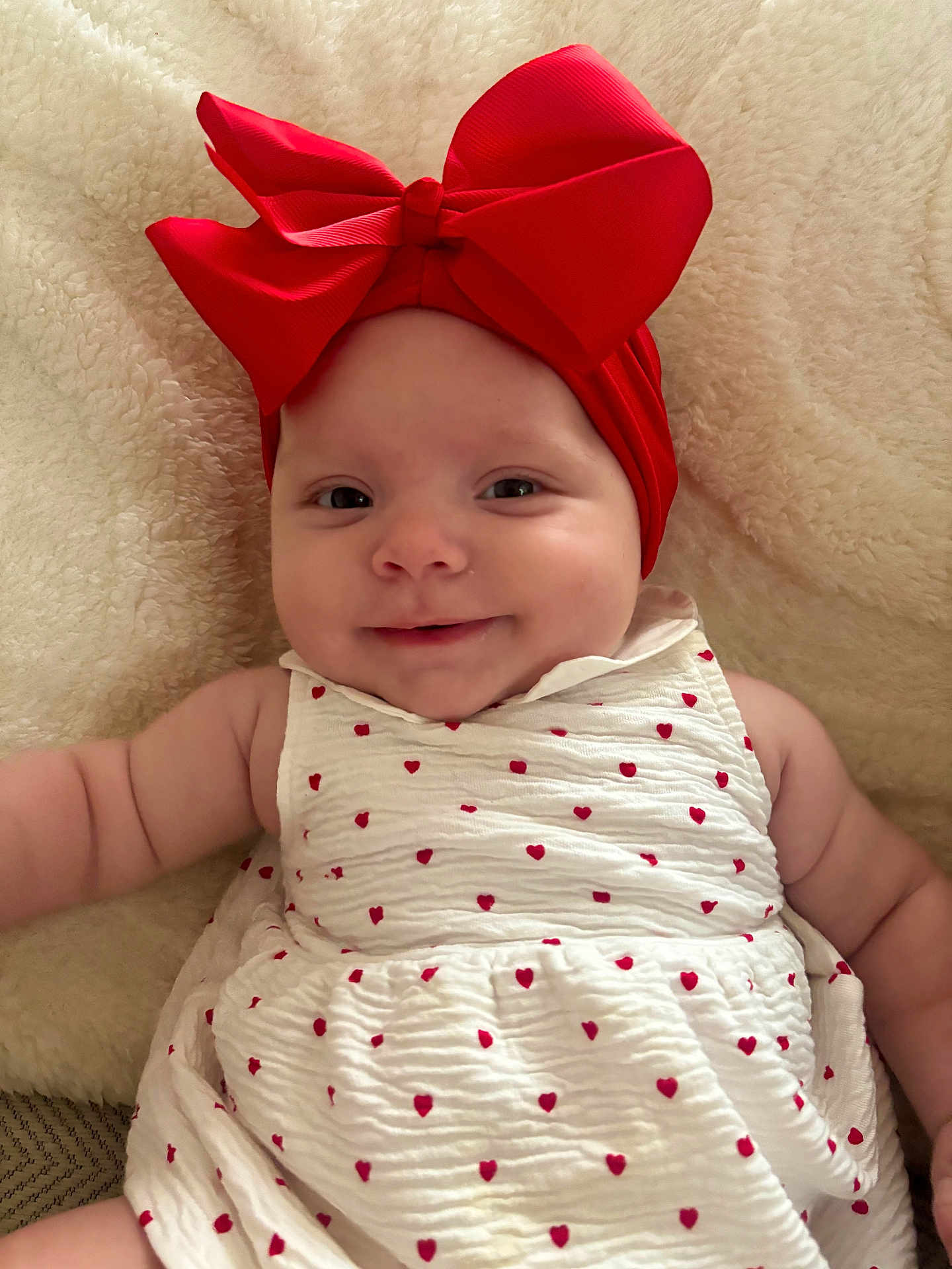 Naëlya participe au concours pour gagner de l'argent avec cette photo : baby, infant, red_bow, headband, white_dress, red_hearts, smile, face, skin, arm, blanket, soft_texture, cute, child, portrait, lying_down, close_up, adorable, happy, young