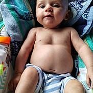 Oryan is registered to the contest to win money with this photo: baby, child, towel, striped_shorts, bare_chest, infant, skin, face, arm, legs, cute, smile, relaxed, indoors, colorful, patterned, fabric, person, young, portrait