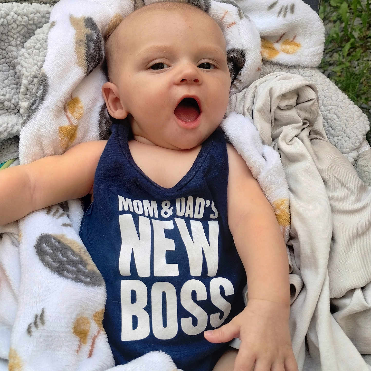 Oryan is registered to the contest to win money with this photo: baby, infant, child, blanket, clothing, face, person, outdoor, nature, expression, tank_top, text_on_clothing, seat, fabric, cute, portrait, young_child, happy, relaxed, resting