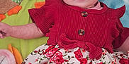 Mathilde participe au concours pour gagner de l'argent avec cette photo : baby, blanket, card, child, clothing, cute, face, floral_pattern, hand, headband, indoors, infant, legs, lying_down, person, plush_toy, red_dress, skin, soft_toy, text