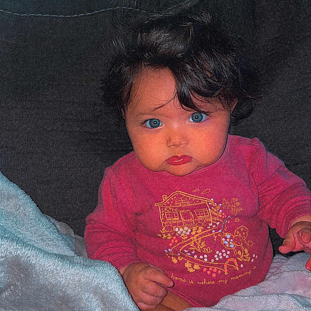 Naziah joined the competition — help win amazing prizes! baby, blanket, blue_eyes, child, clothing, comfort, couch, cozy, curly_hair, expression, face, home, hope, indoor, person, pink_shirt, portrait, seated, text, young_child